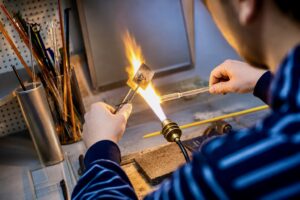 Skilled glassblower shaping high-purity quartz tubing with a hand torch. Made in USA TCS Technologies UV curing lamp.